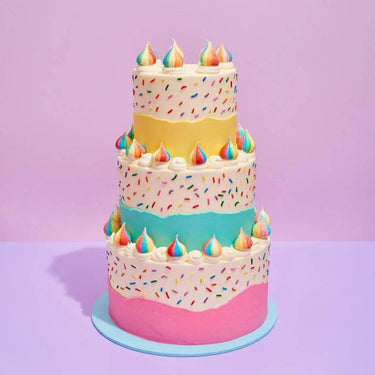 Birthday Cake by Crumbs & Doilies with three colorful tiers, rainbow sprinkles, and unicorn poop meringue decorations.